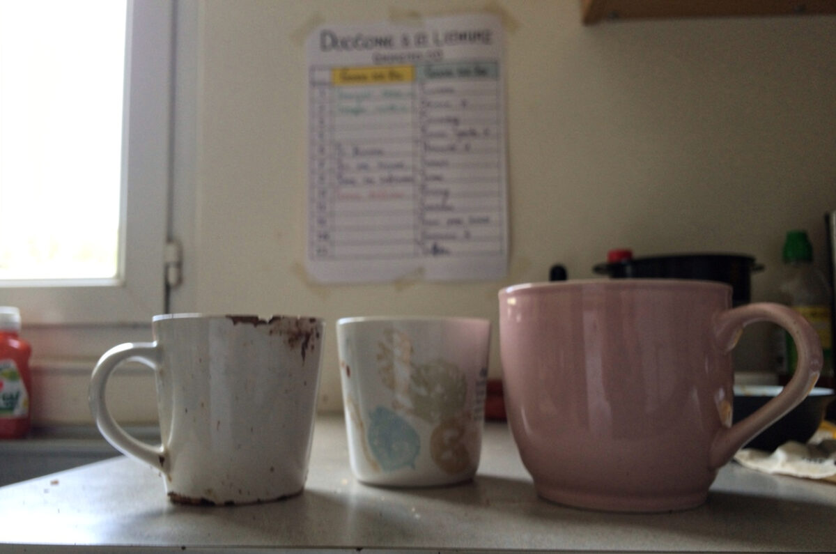 Trois tasses dépareillées et un tableau de répartition des tâches dans une cuisine de colocation