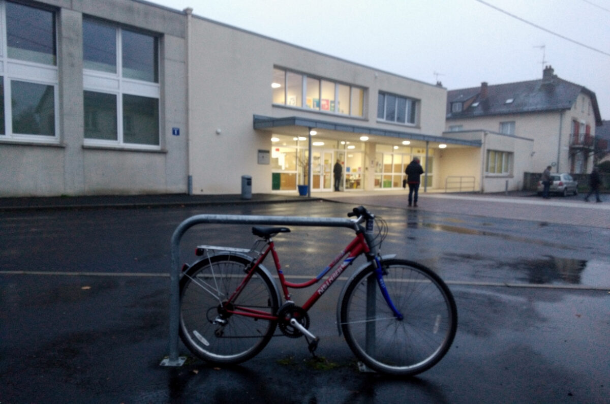 Vélo attaché à un râtelier devant un bâtiment d'enseignement un matin gris