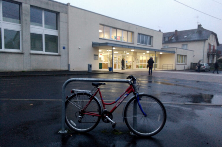Vélo attaché à un râtelier devant un bâtiment d'enseignement un matin gris
